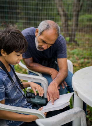 boy with binoculars looking through a book, a man is pointing at a page